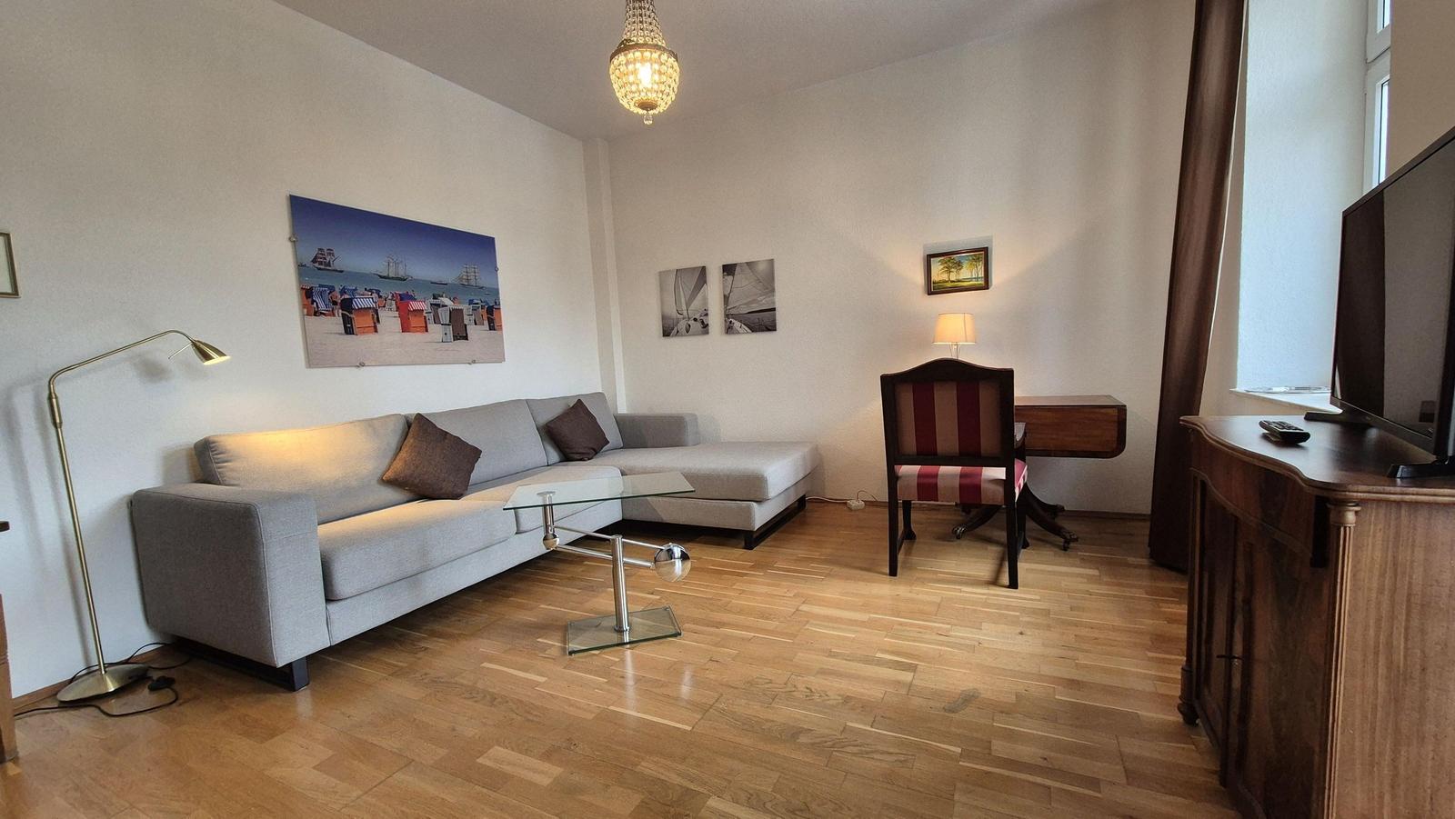 Wohnzimmer mit Sofa, Couchtisch und Schreibtisch. Holzboden und Wandbilder.