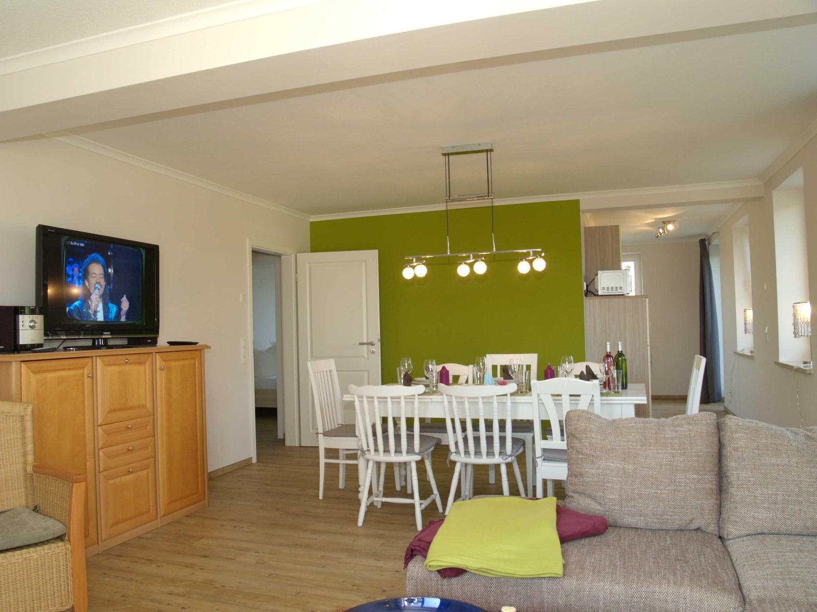 Wohn- und Essbereich mit grüner Wand, weißem Tisch und Sofa mit Kissen.