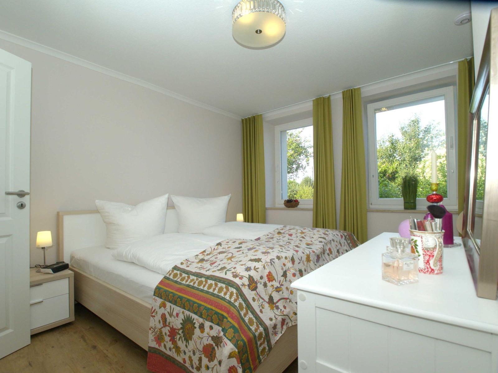 Schlafzimmer mit Doppelbett, grünen Vorhängen und Fensterblick auf Grünflächen.