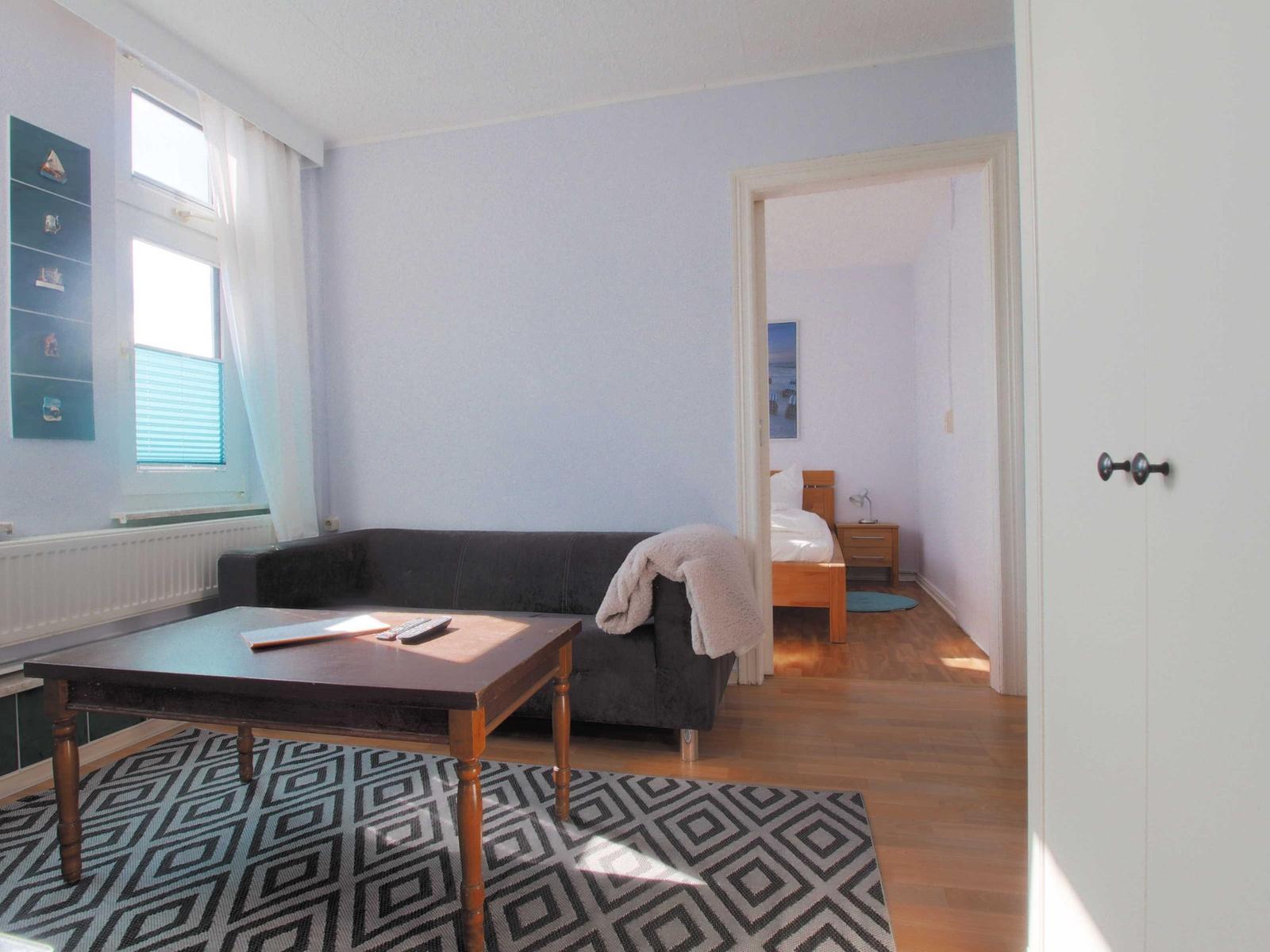 Wohnzimmer mit Sofa, Tisch und Blick in Schlafzimmer mit Bett.