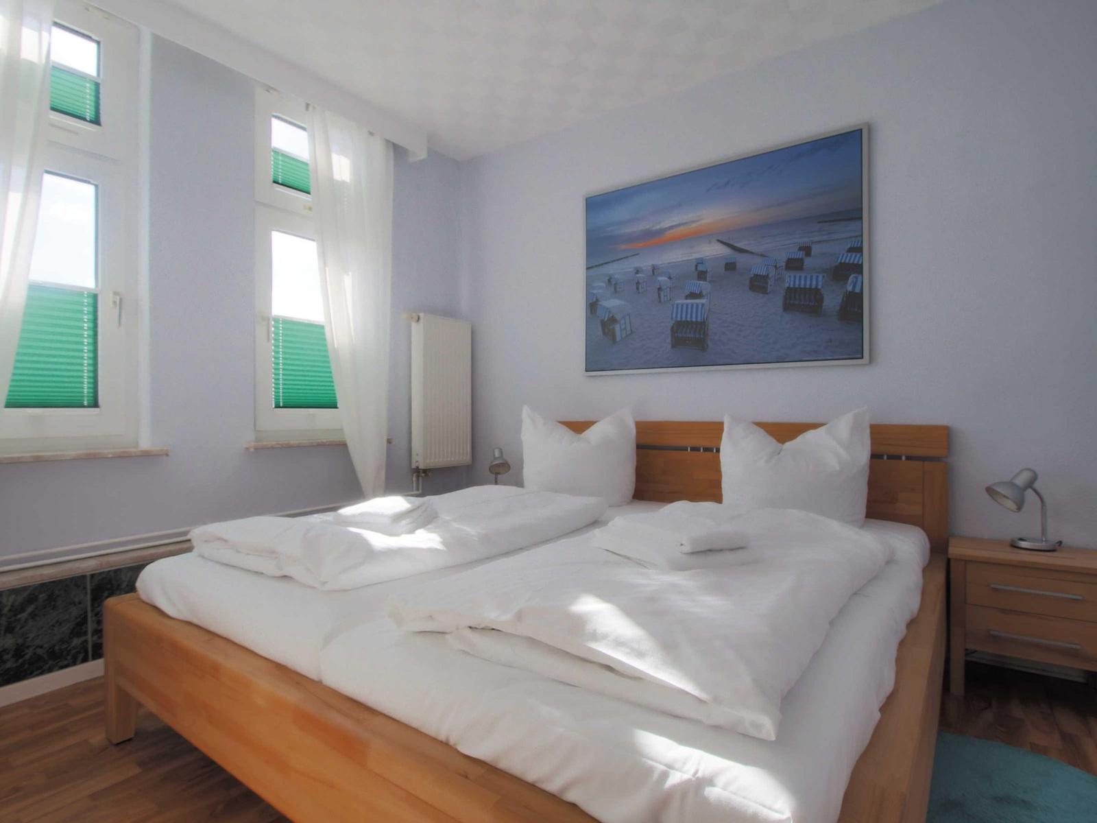 Schlafzimmer mit Bett, Nachttisch und Wandbild. Fenster mit grünen Jalousien.