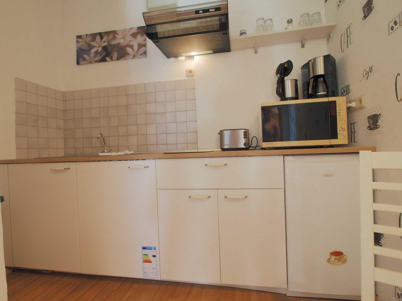 Küche mit weißen Schränken, Mikrowelle, Kaffeemaschine und Spüle.