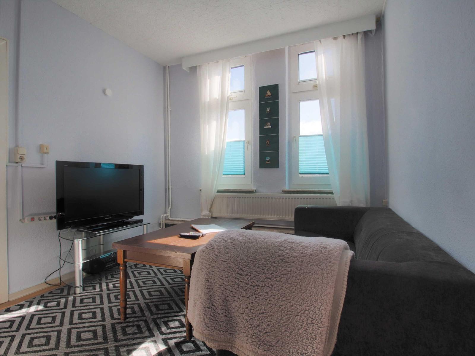 Wohnzimmer mit Sofa, Fernseher und Fenster mit Vorhängen.