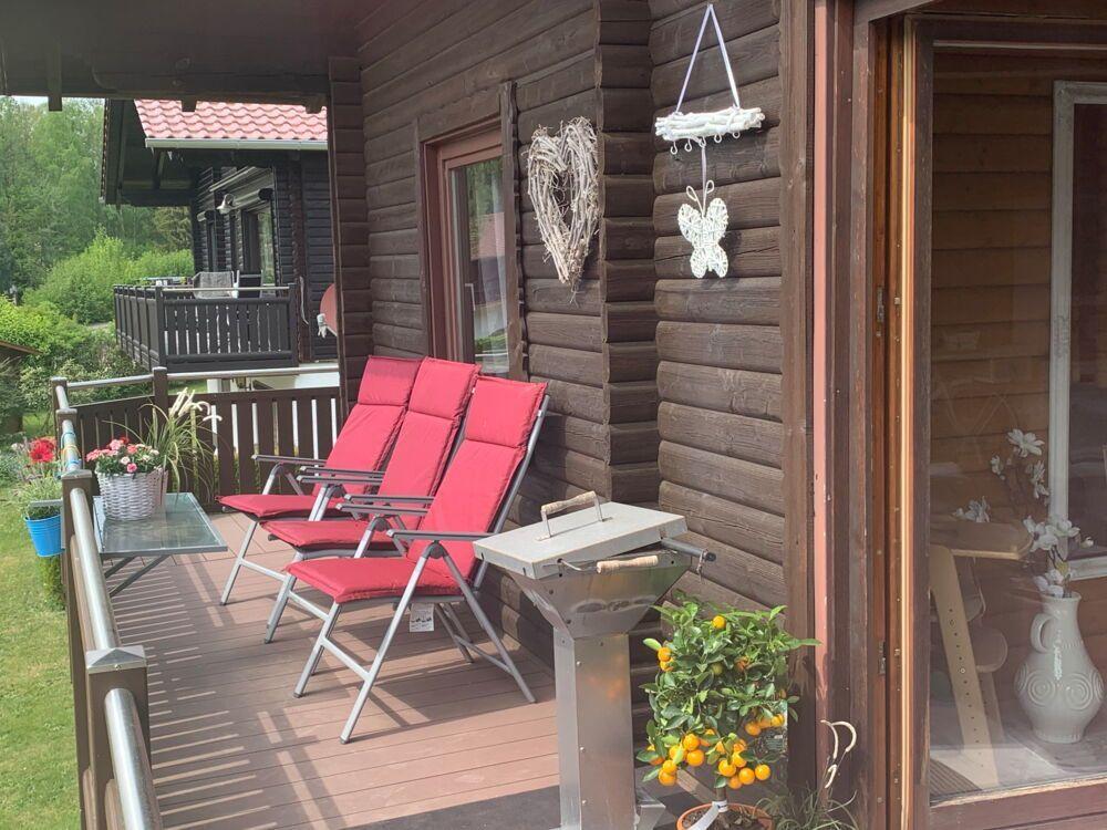 Deck with two red chairs, grill, and plants in front of a wooden house.