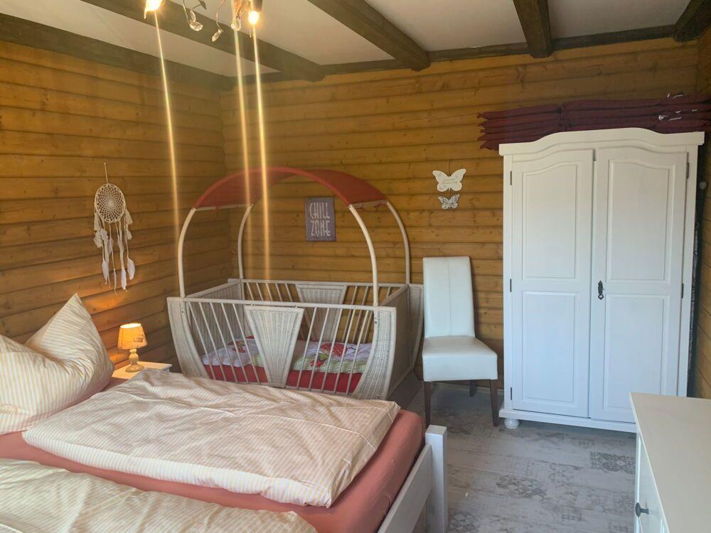 Bedroom with bed, cot, and wardrobe. Wooden walls and ceiling beams.