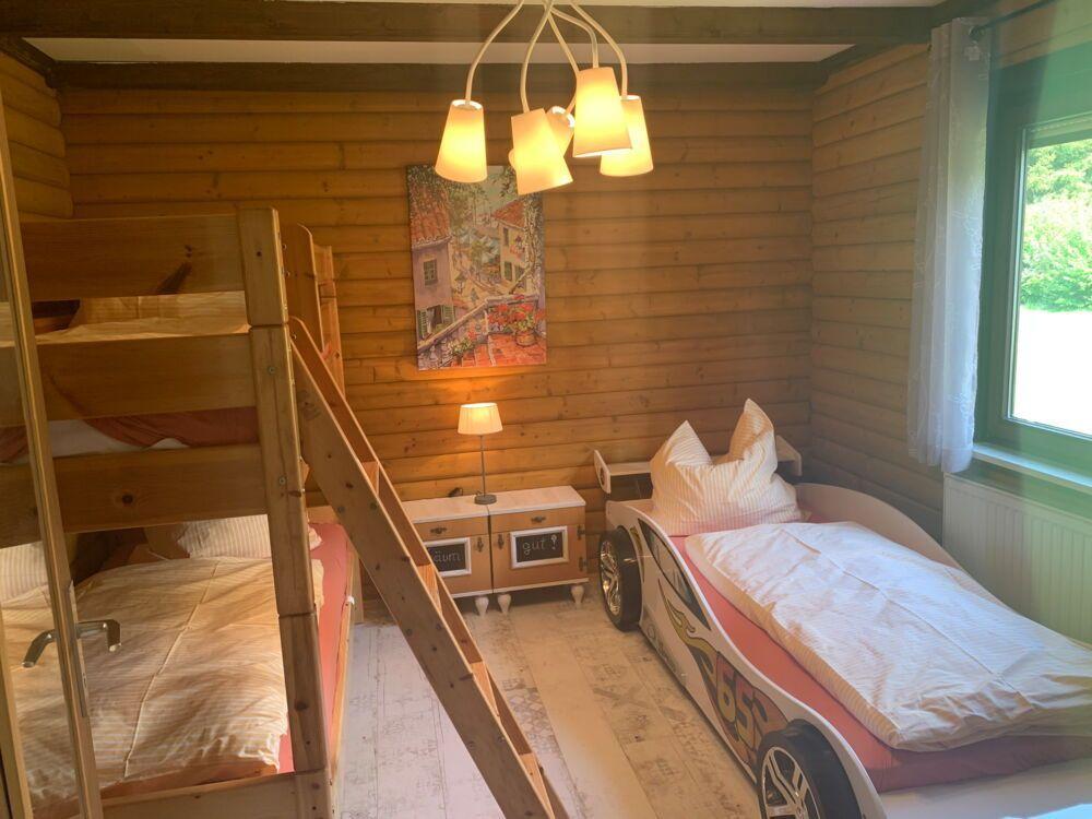 Room with bunk bed and car bed, wood wall, window and ceiling light.