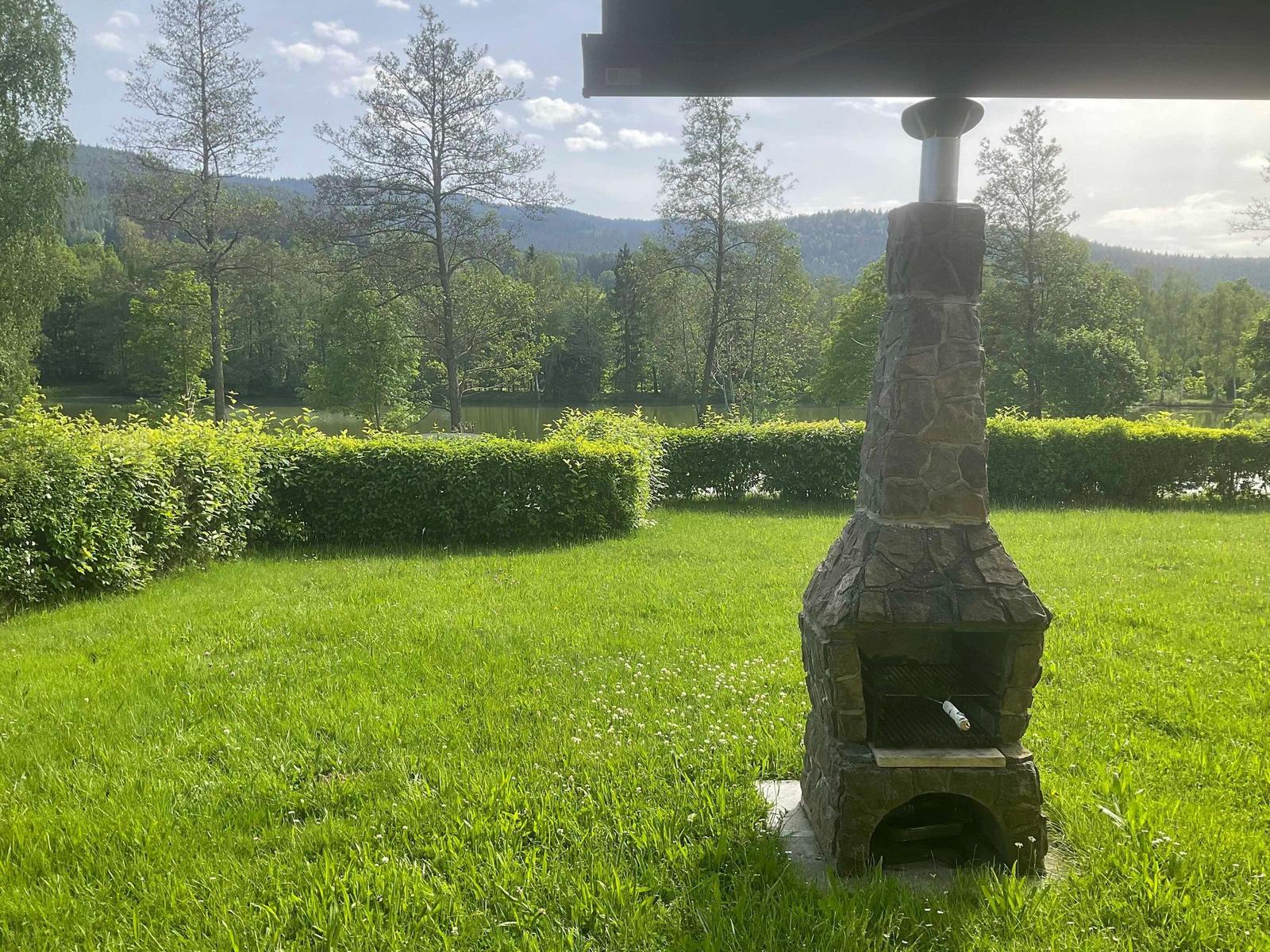 Stone oven on green lawn with view of forest and lake.