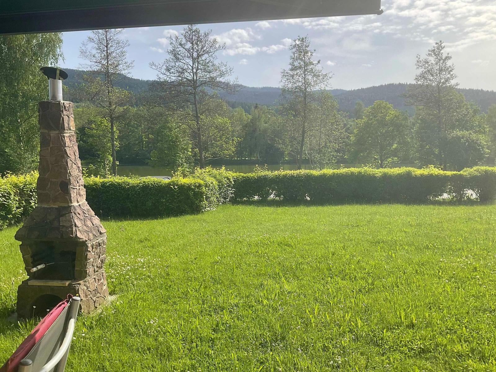 Green lawn with stone fireplace and view of forest and lake.