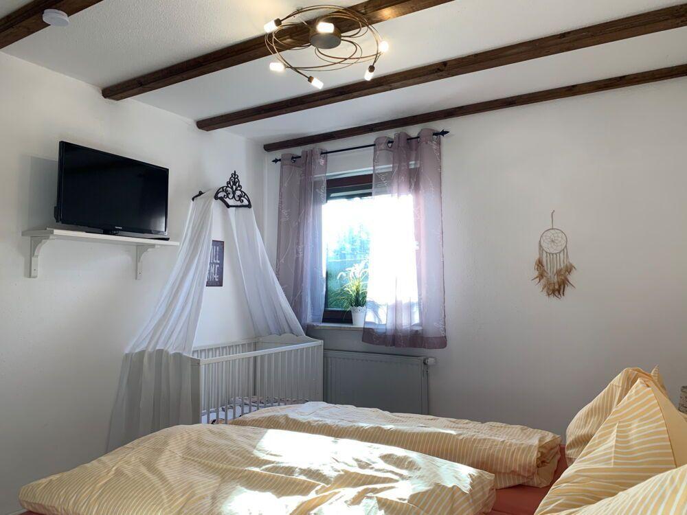 Bedroom with crib, TV, and window with curtains.