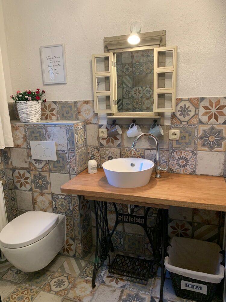 Bathroom with sink on sewing machine stand, colorful tiles, and mirror cabinet.