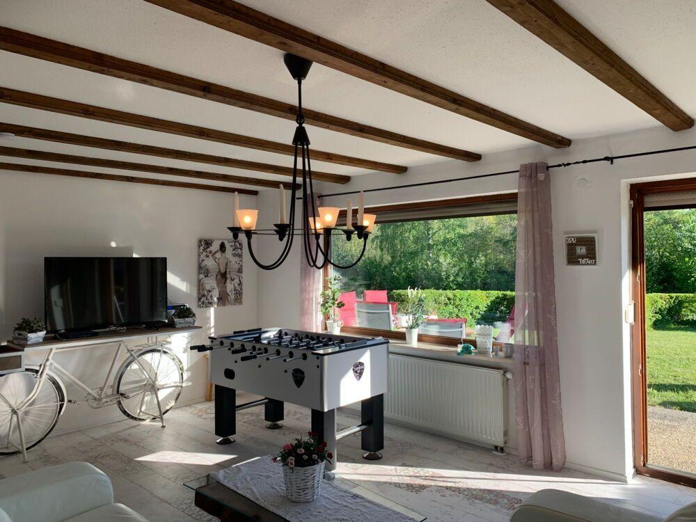 Living room with foosball table, TV, and bicycle. Doorway to terrace with garden view.