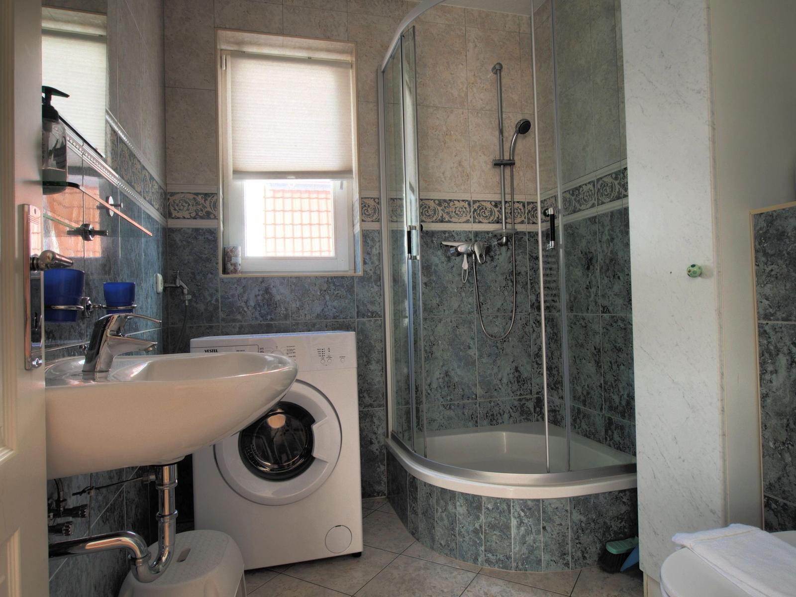 Badezimmer mit Dusche, Waschmaschine und Waschbecken