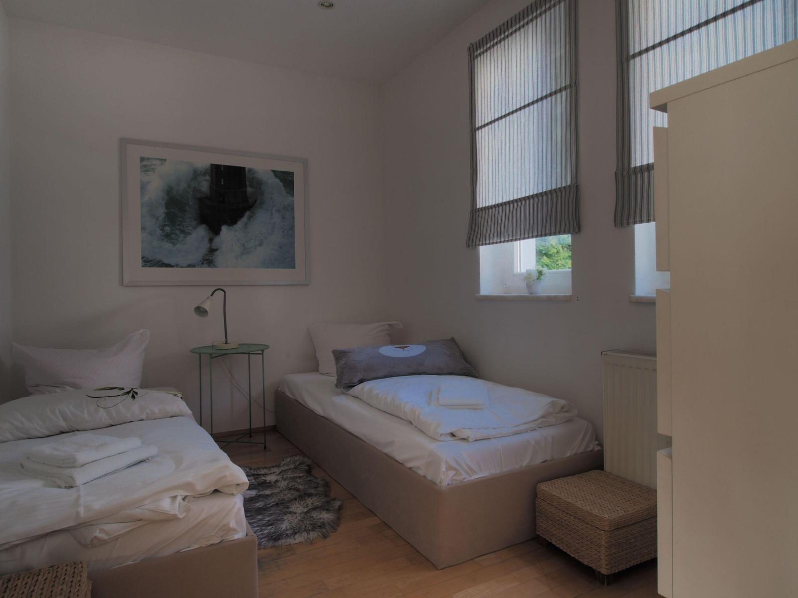 Zwei Betten, Fenster mit Jalousien, Wandbild, Nachttisch und Teppich.