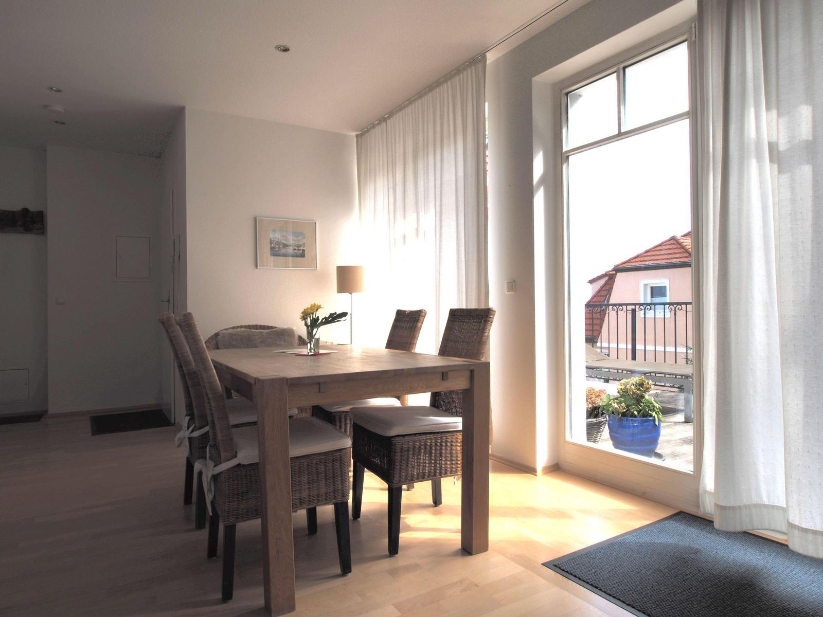Esszimmer mit Holztisch, Stühlen und Balkonansicht.