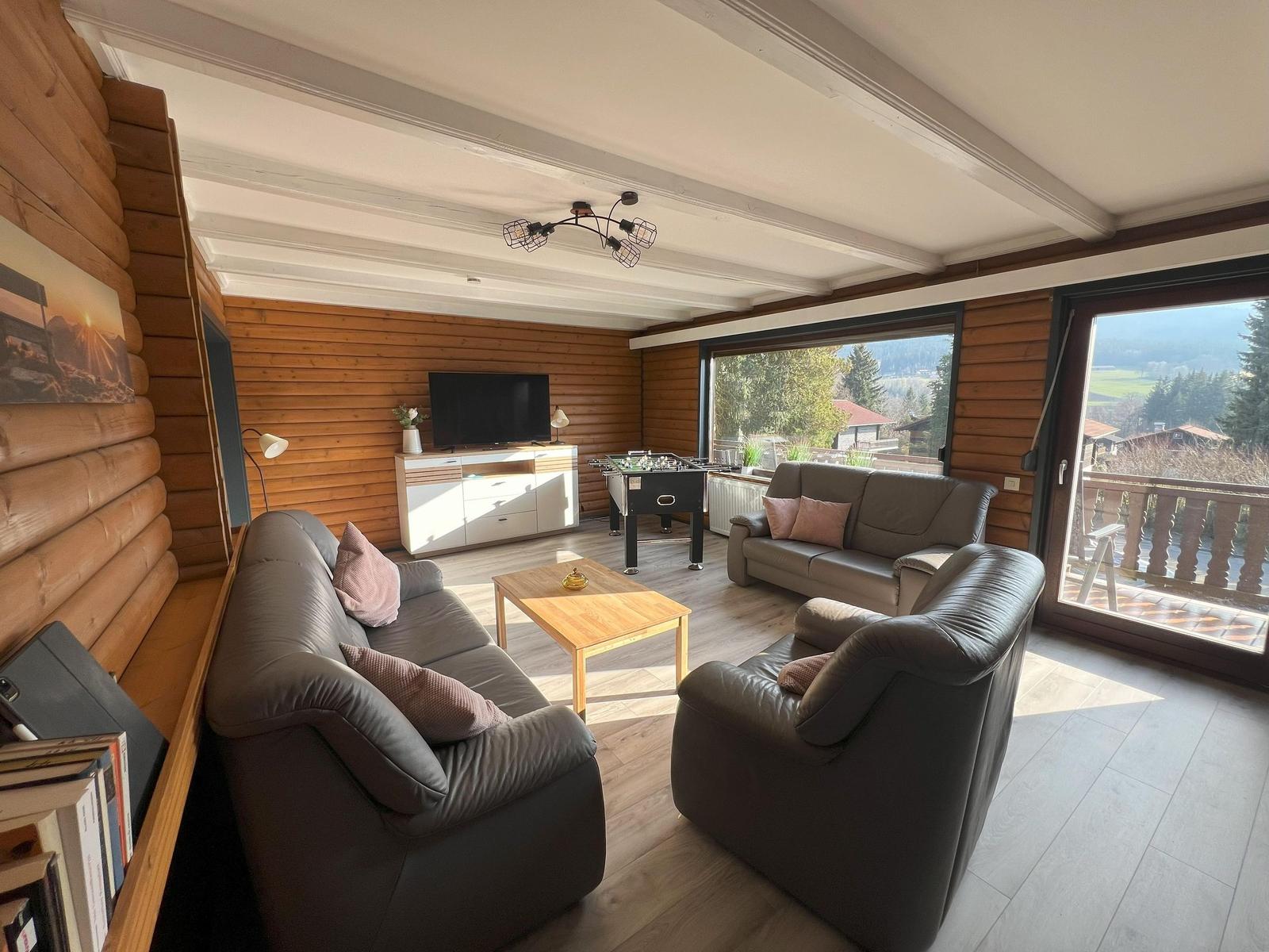 Living room with sofa, armchair, TV, and view of balcony and landscape.