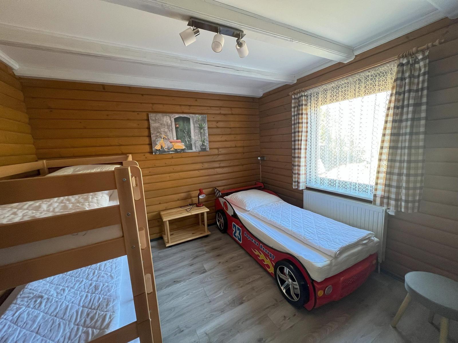 Room with bunk bed and race car bed, wooden walls and window with curtains.