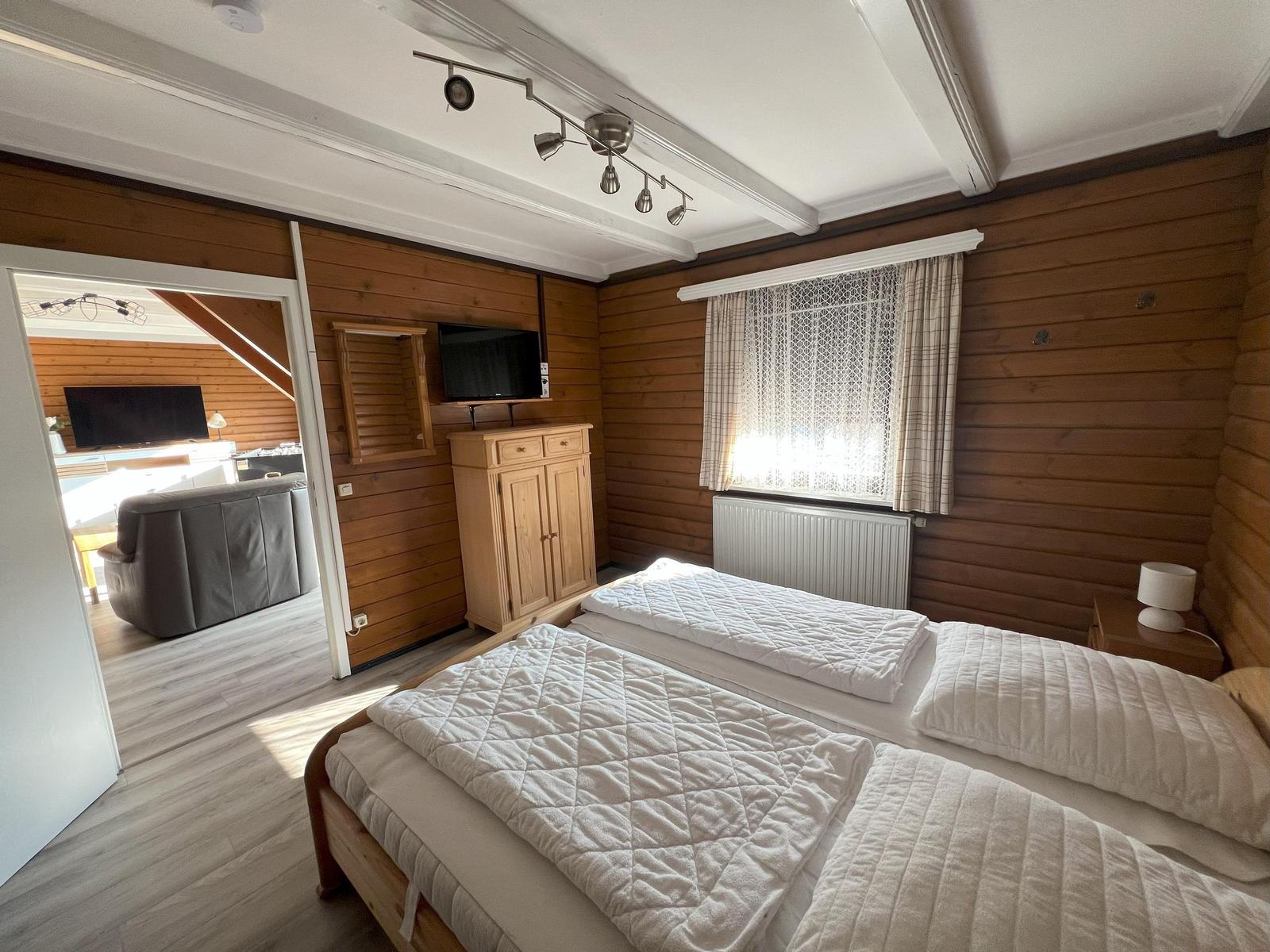 Bedroom with double bed, wood walls, and TV. Passage to living room.