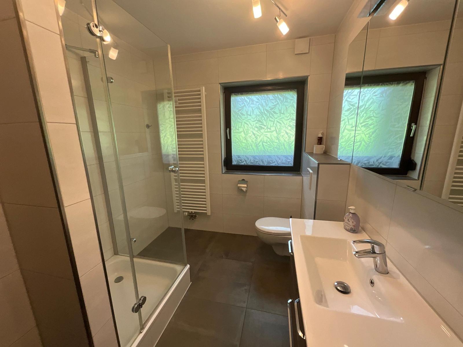 Bathroom with shower, toilet, and sink. Window with green pattern.