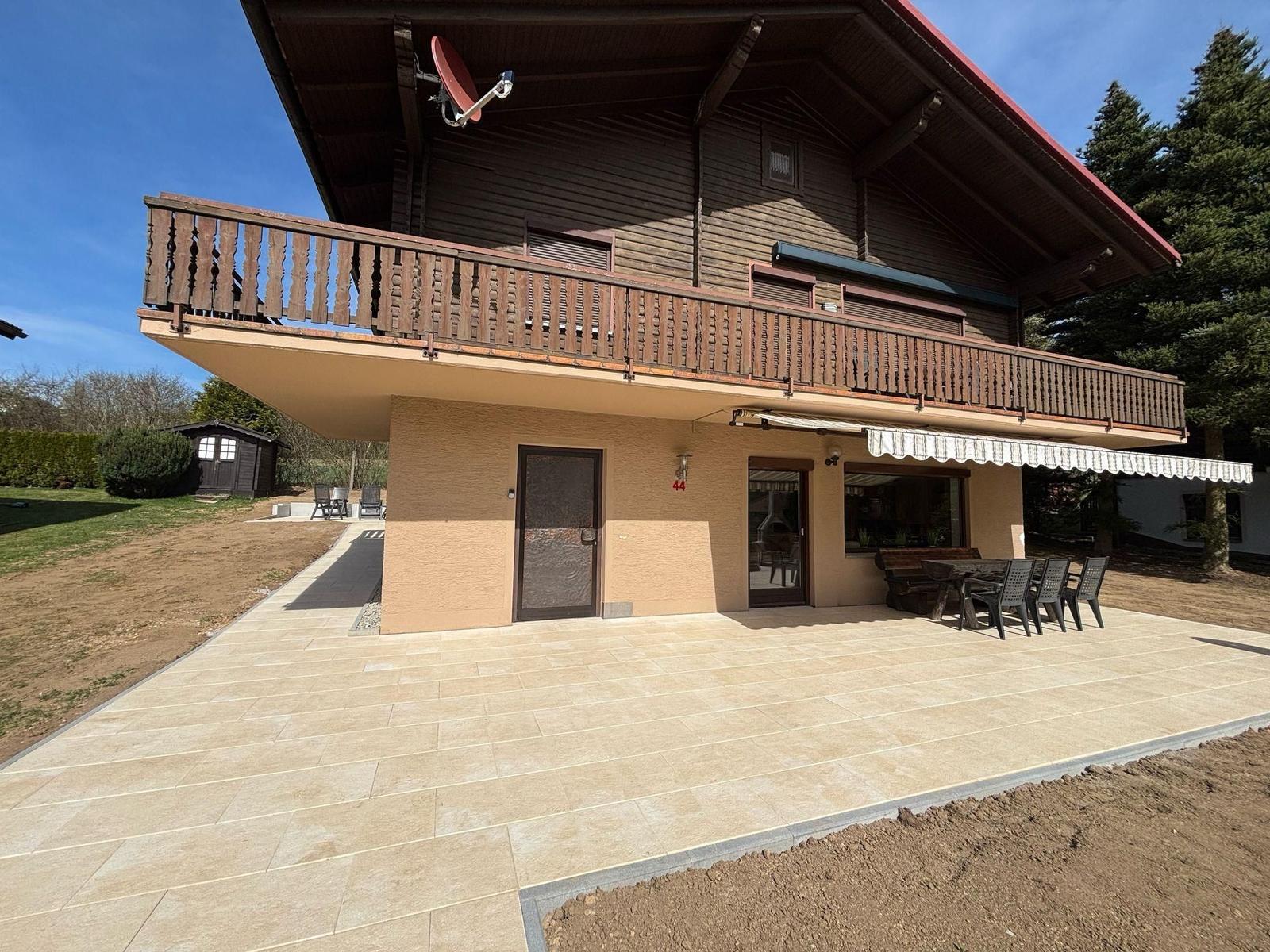House with terrace, balcony, and garden area under blue sky.