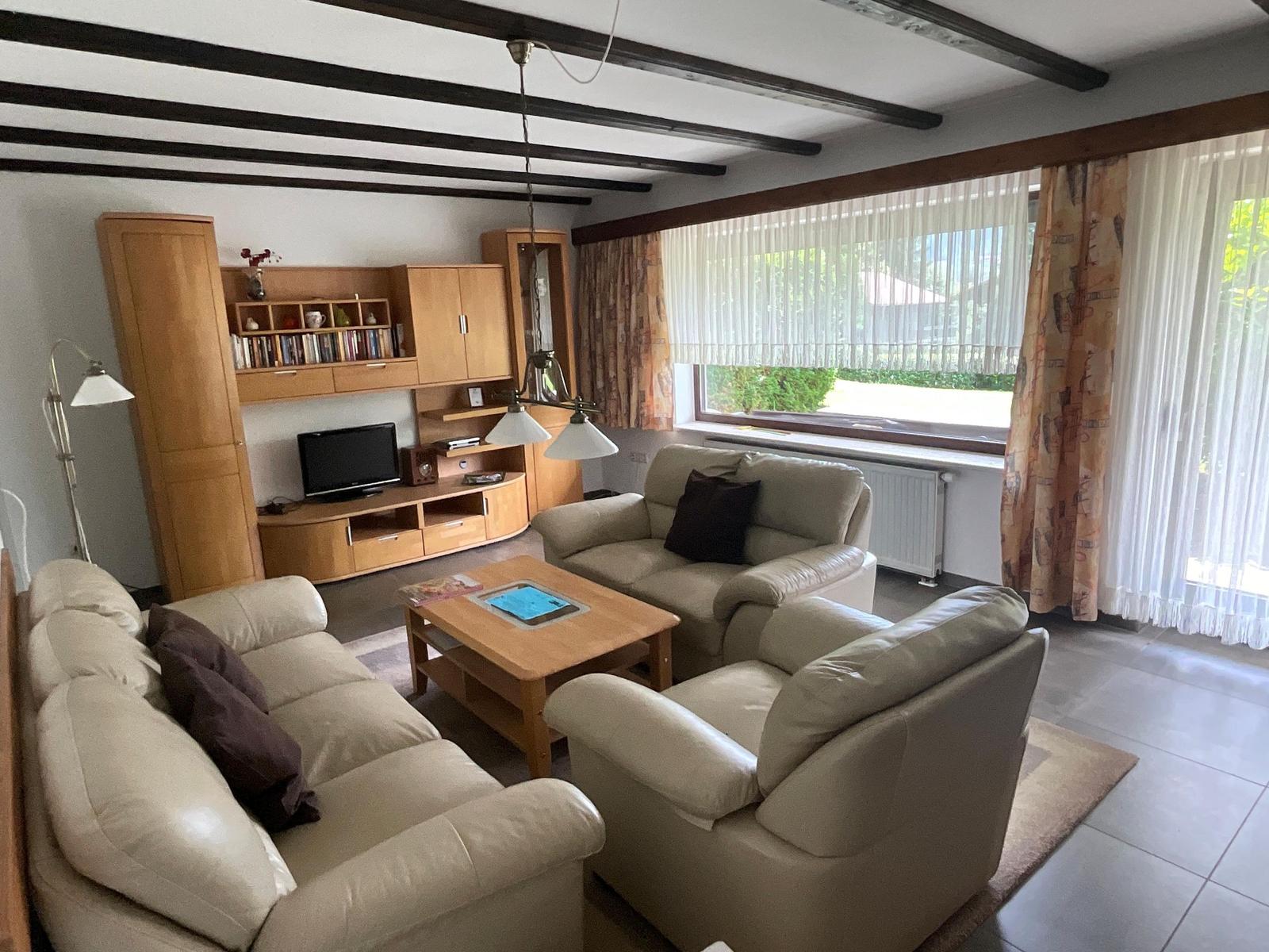 Living room with leather sofa, wooden furniture, and large windows.