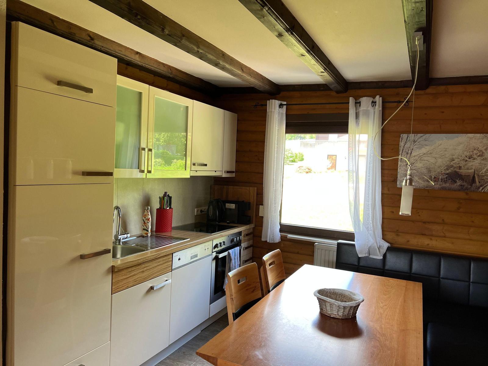 Kitchen with dining area, wooden walls, and window. Table, chairs, and appliances are visible.