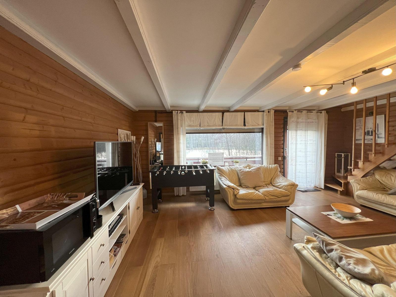 Living room with sofa, foosball table, and TV. Wooden walls and floor. Window with view.