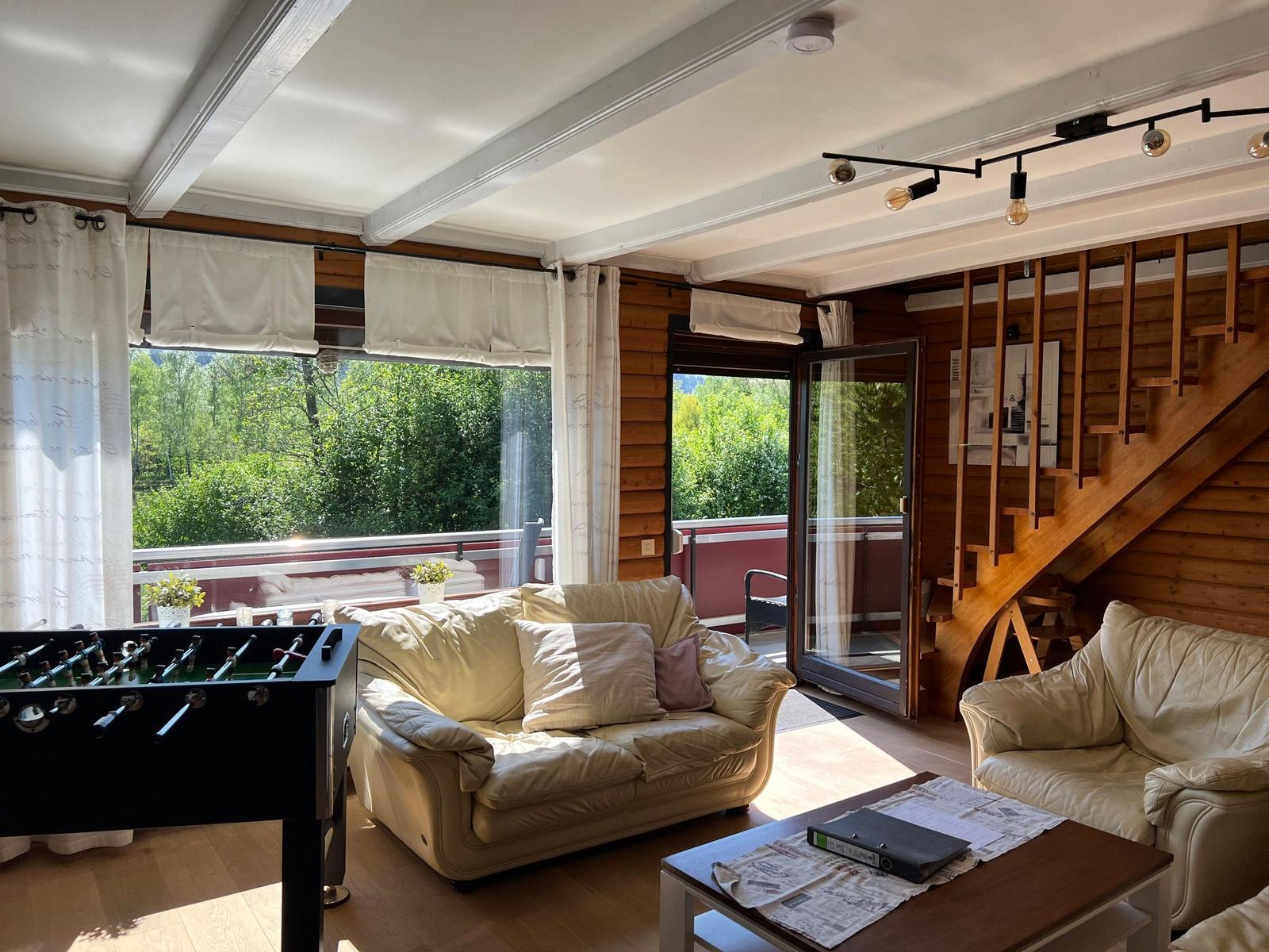 Living room with sofa, table football, and balcony view. Wooden stairs lead upstairs.