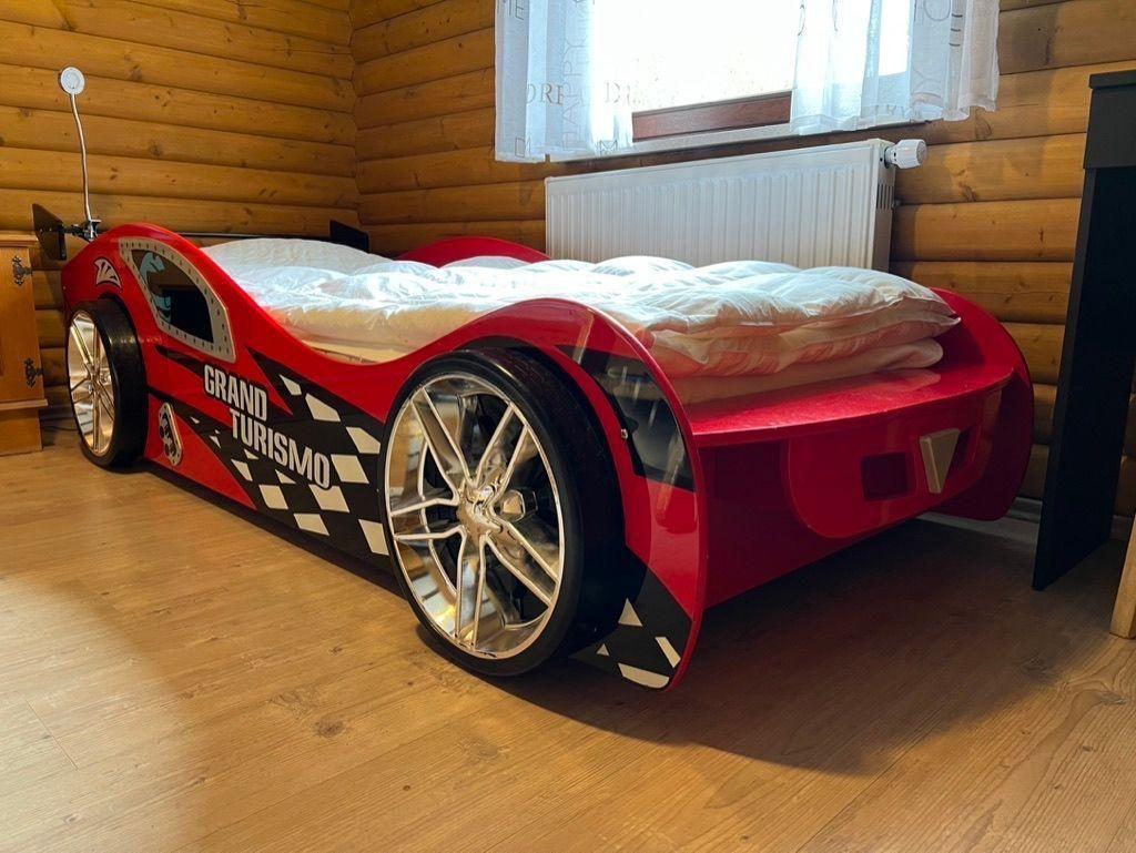 A red race car bed with white linens is in a wooden house room.