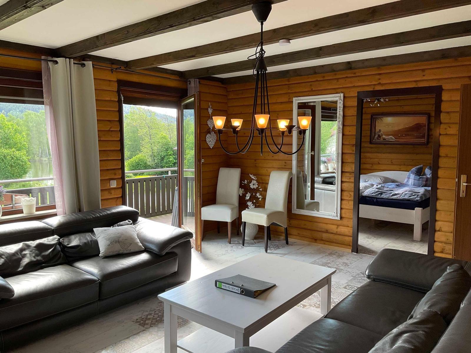 Living room with sofa, table, and view of balcony and forest.