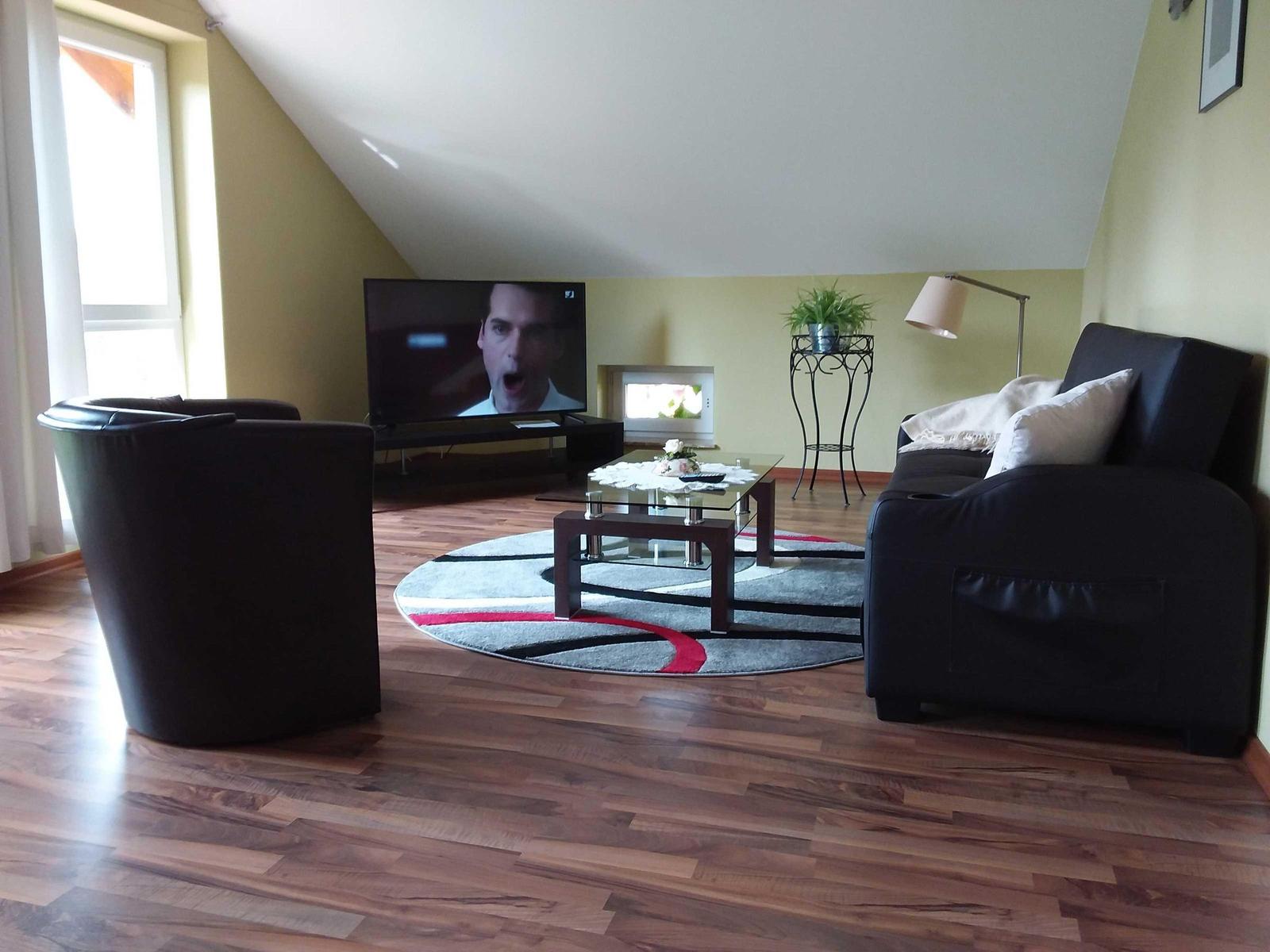 Wohnzimmer mit Sofa, Sessel, Fernseher und Holzboden.