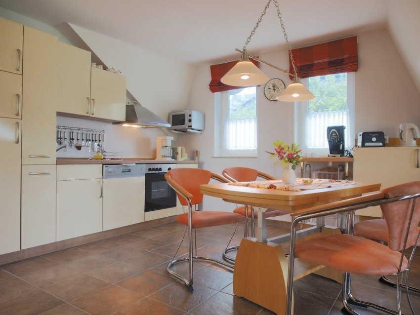 Küche mit Essbereich, Holztisch, orangefarbenen Stühlen und Fenstern mit roten Rollos.