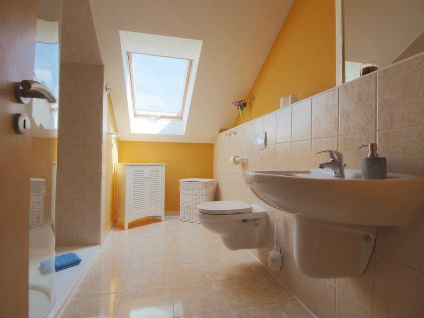 Badezimmer mit Dusche, Toilette und Waschbecken unter Dachschrägen mit Dachfenster.