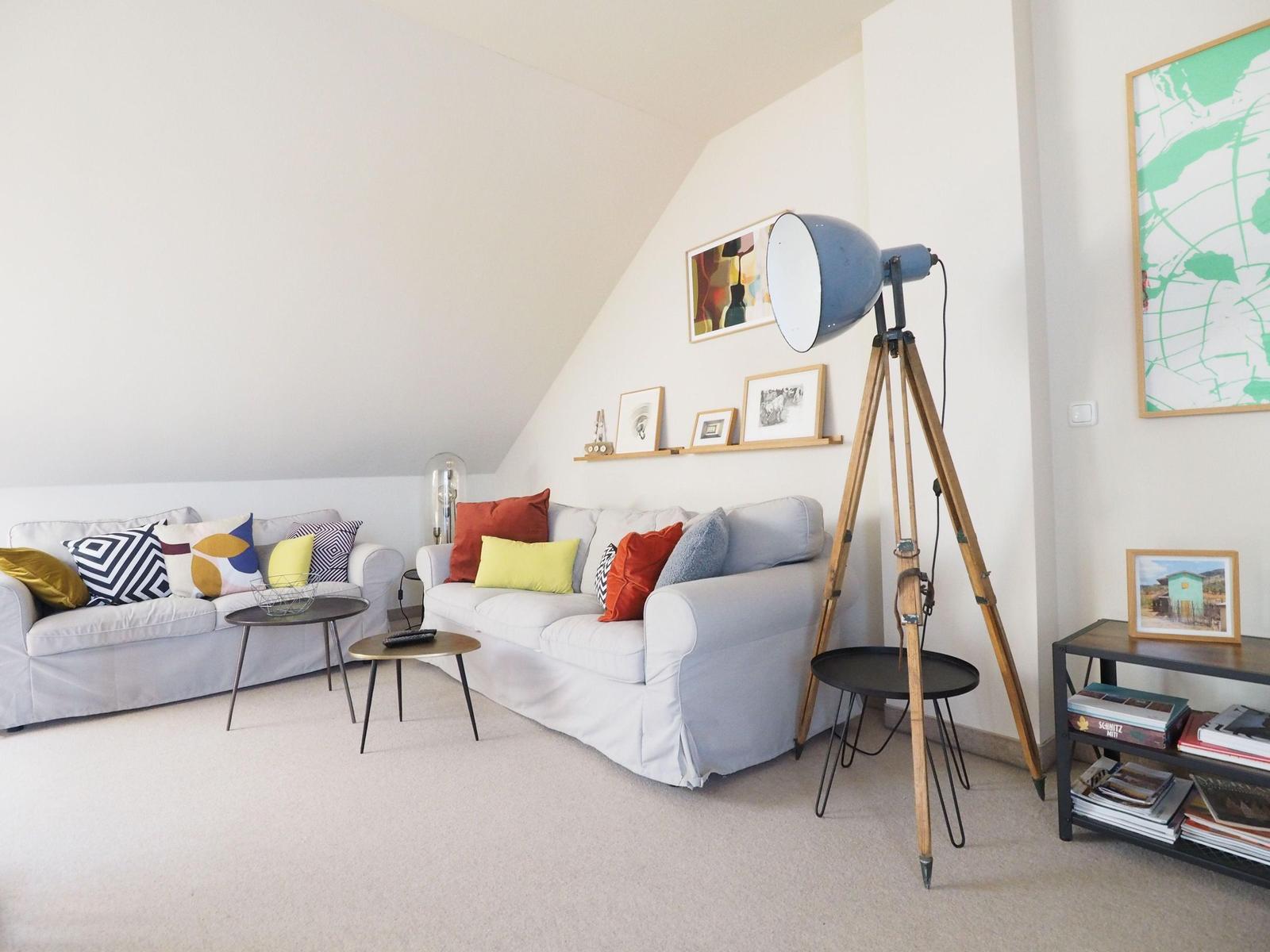Zwei Sofas mit Kissen, Stehlampe, Tische und Wandbilder in einem Raum mit schräger Decke.