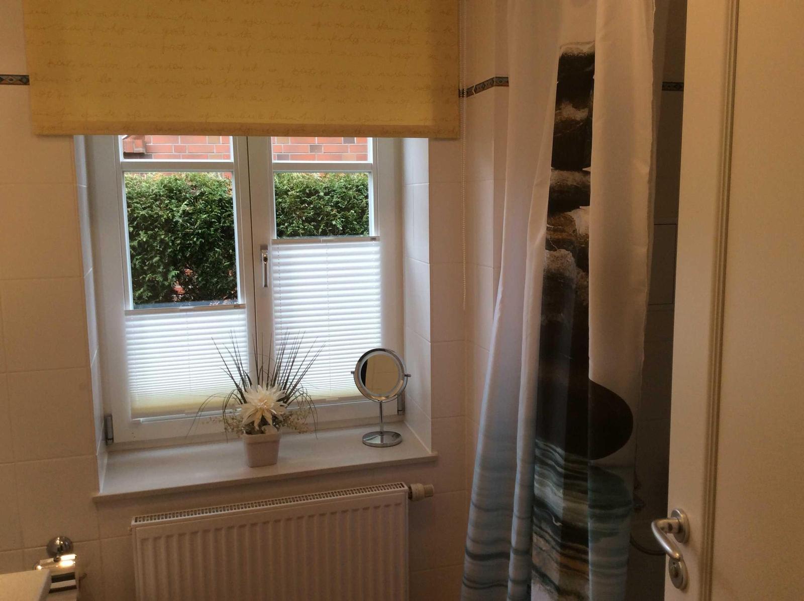 Badezimmer mit Fenster, Heizkörper und Duschvorhang.