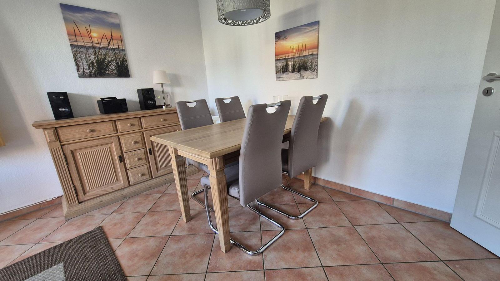 Esszimmer mit Holztisch, Stühlen und Sideboard. Wandbilder und Deckenleuchte.