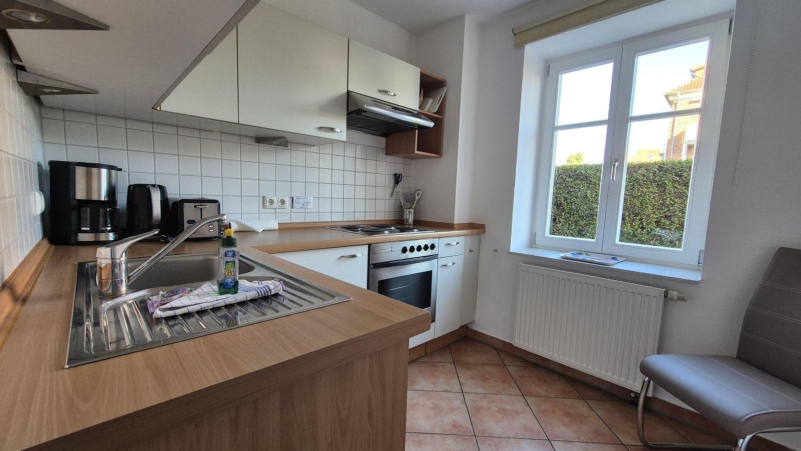 Küche mit Arbeitsplatte, Spüle, Herd und Fenster mit Blick auf Hecke.