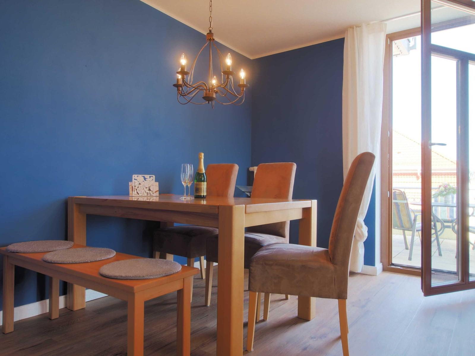 Esszimmer mit Holztisch, Stühlen und Bank. Blaue Wände und Glastür zum Balkon.