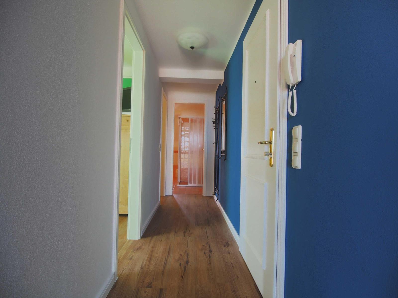 Flur mit Holzboden, blauer Wand und weißen Türen. An der Wand hängt ein Telefon.