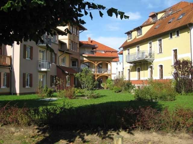Hof mit mehreren Häusern, grüner Rasen und Bäumen im Hintergrund.