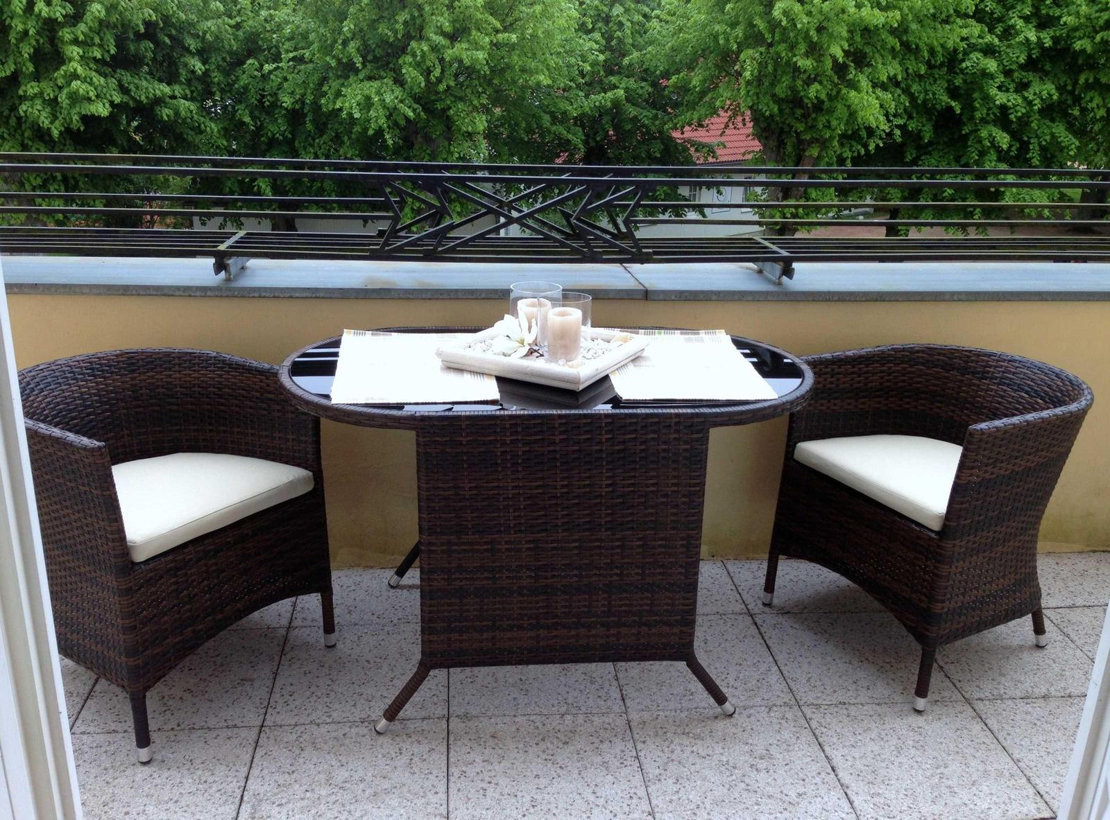 Terrasse mit runden Tisch und zwei Stühlen, weißer Sitzauflage, Tischdekoration und Blick auf Bäume.