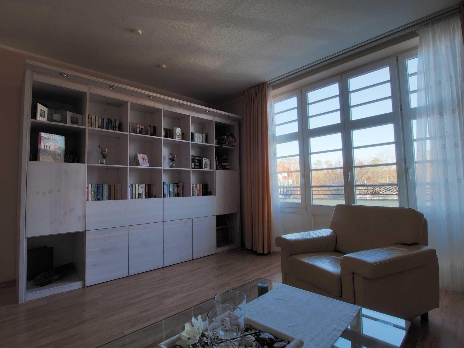 Wohnzimmer mit Bücherregal, Ledersofa und Glas-Tisch. Große Fenster mit Blick auf Balkon.