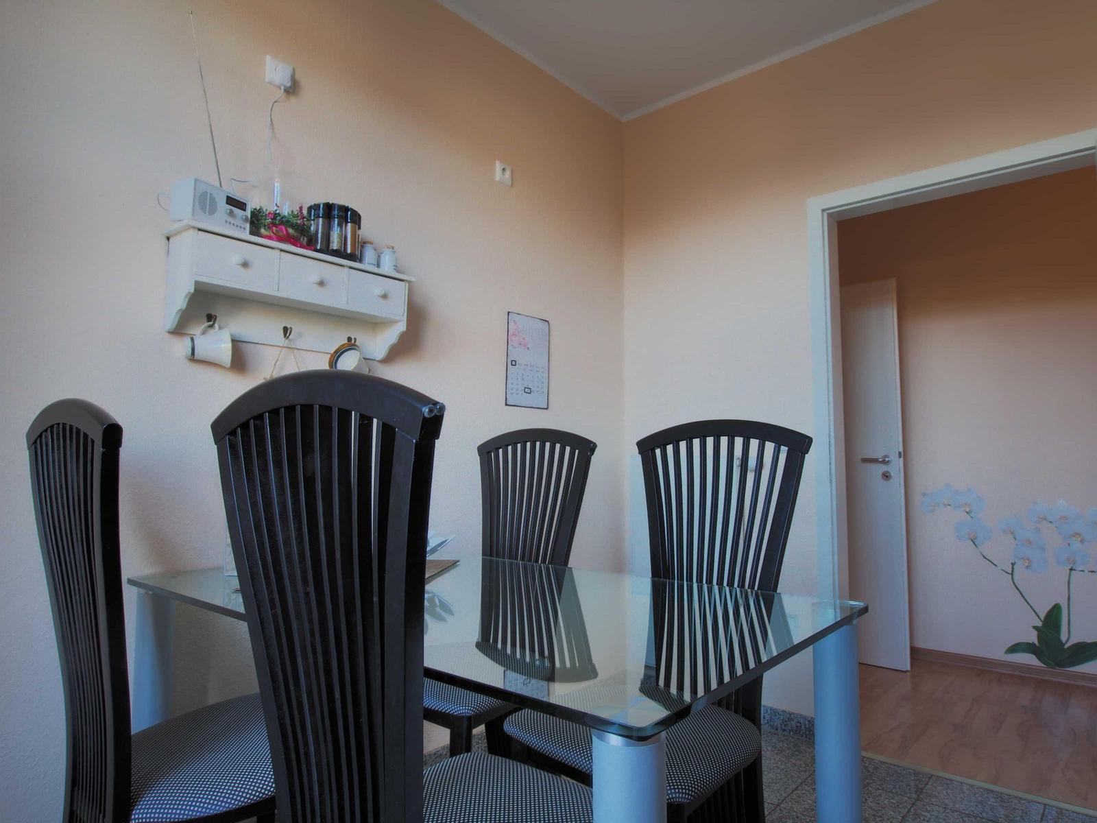 Esszimmer mit Glas-Tisch und vier Stühlen, Wandregal und Kalender an der Wand.