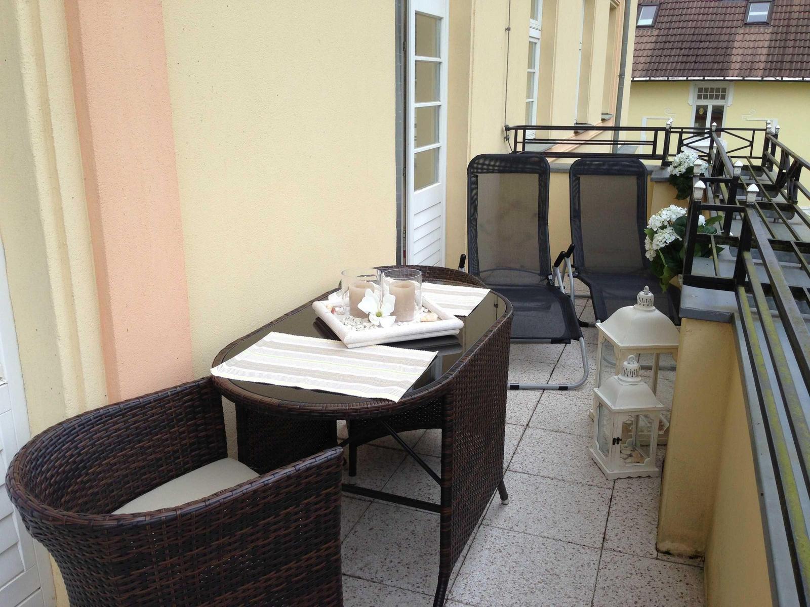 Terrasse mit Tisch, Stühlen und Gartenmöbeln. Weiße Laterne und Blumen dekorieren den Außenbereich.