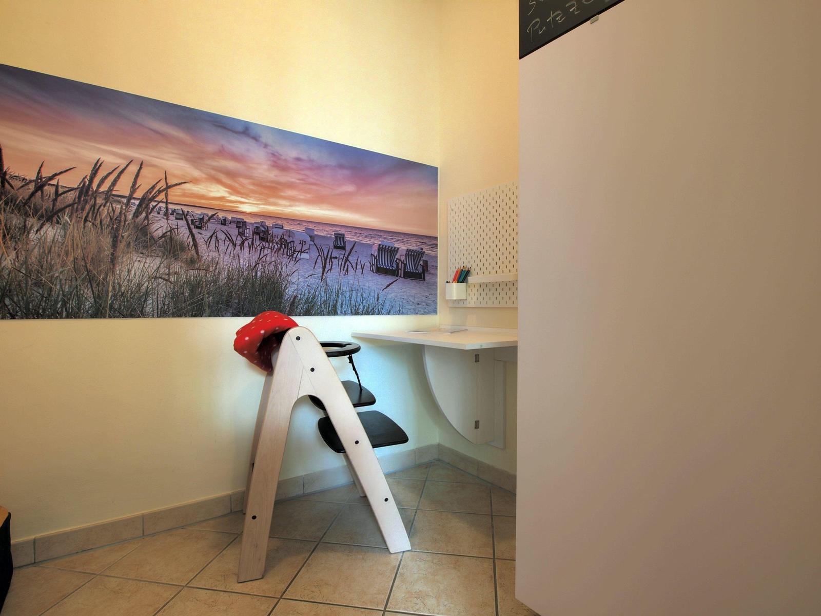 Kinderzimmer mit Hochstuhl, Schreibtisch und Strandbild an der Wand.