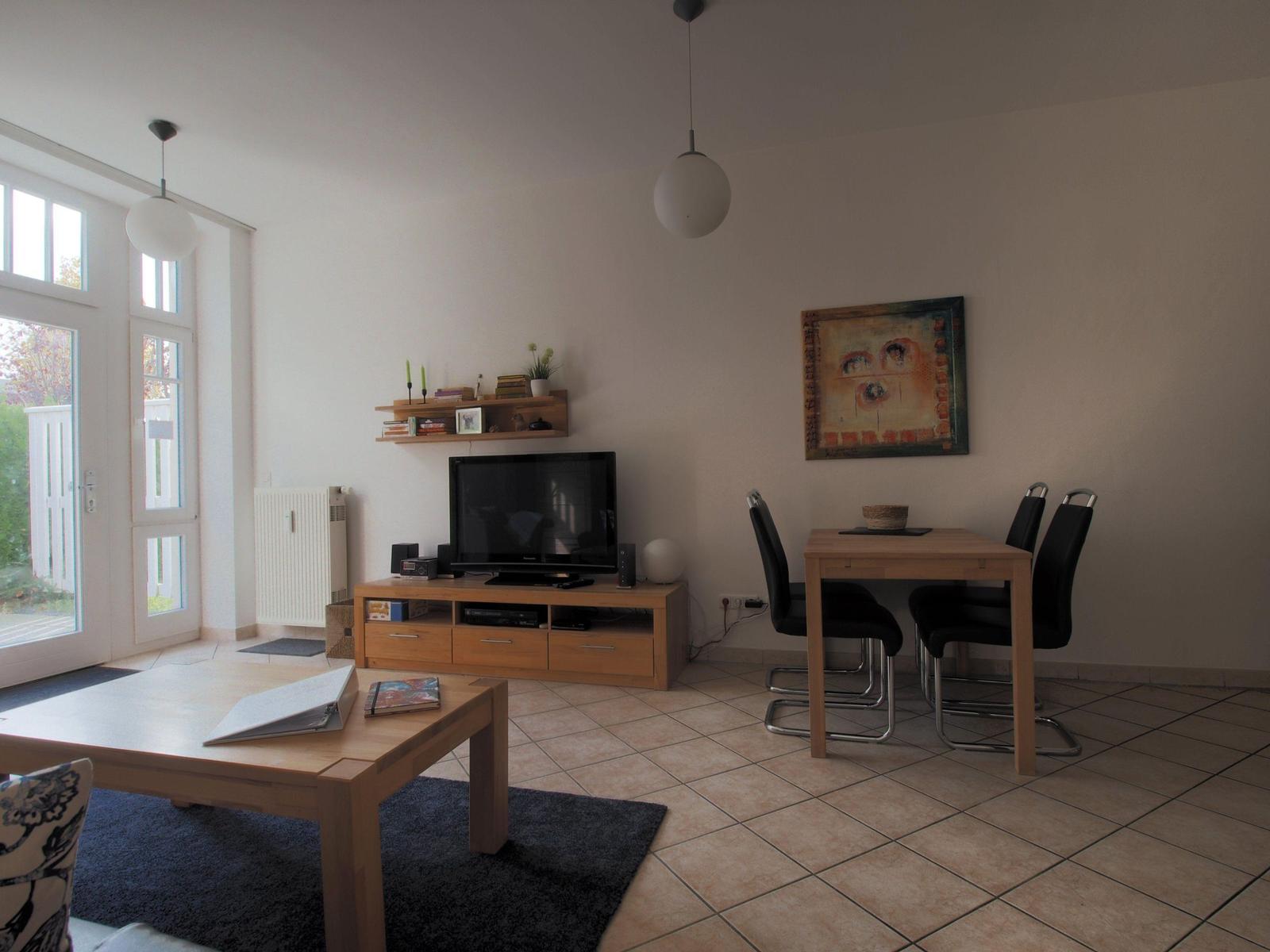 Wohn- und Essbereich mit TV, Esstisch und Fenster zur Außenterrasse.