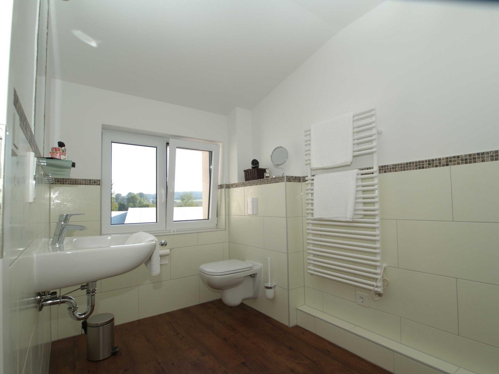 Badezimmer mit Waschbecken, Toilette und Heizkörper. Fenster mit Blick auf Landschaft.