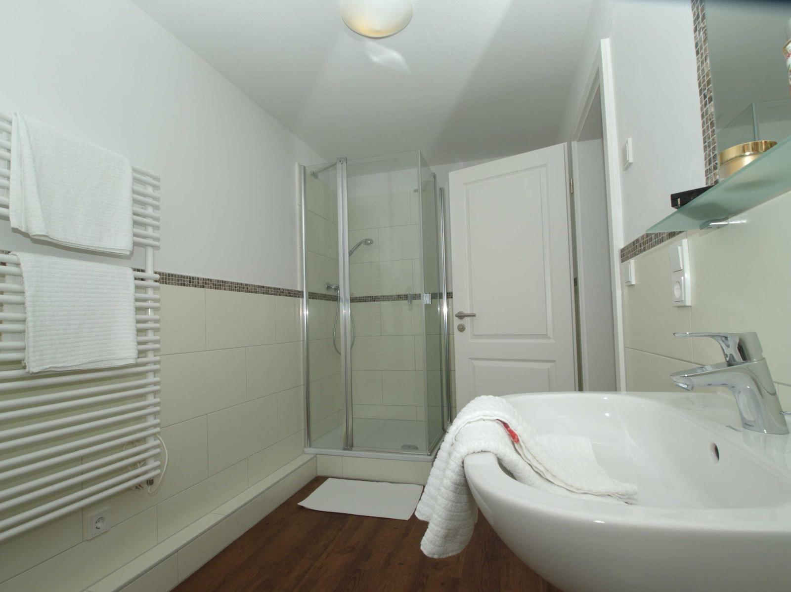 Badezimmer mit Dusche, Waschbecken und Heizkörper. Holzfußboden und weiße Wände.