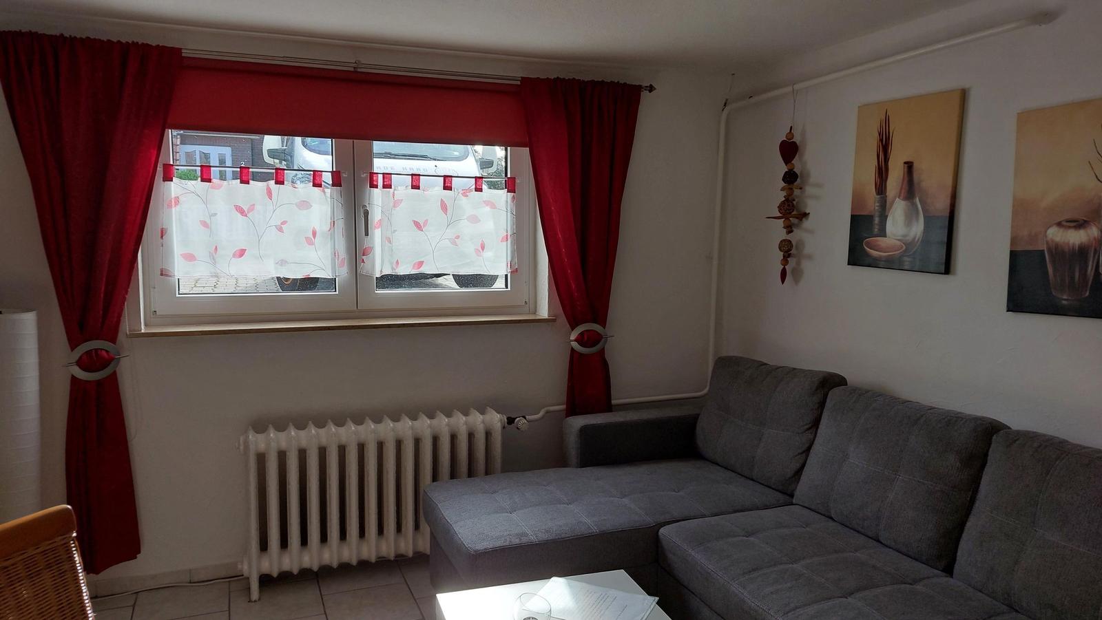 Ein Wohnzimmer mit grauem Sofa, roten Vorhängen und zwei Wandbildern.