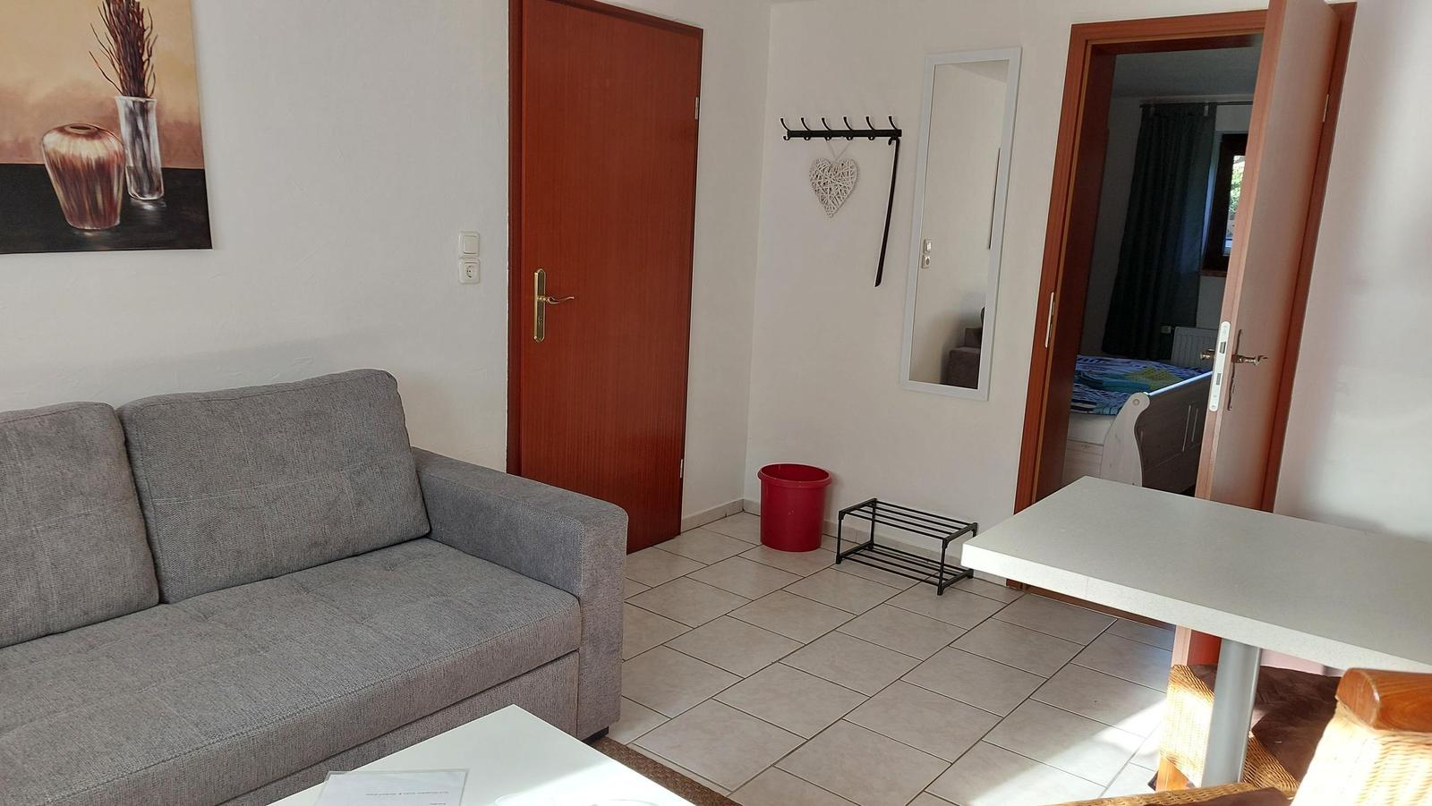 Wohnzimmer mit Sofa, Tisch und Blick in Schlafzimmer.