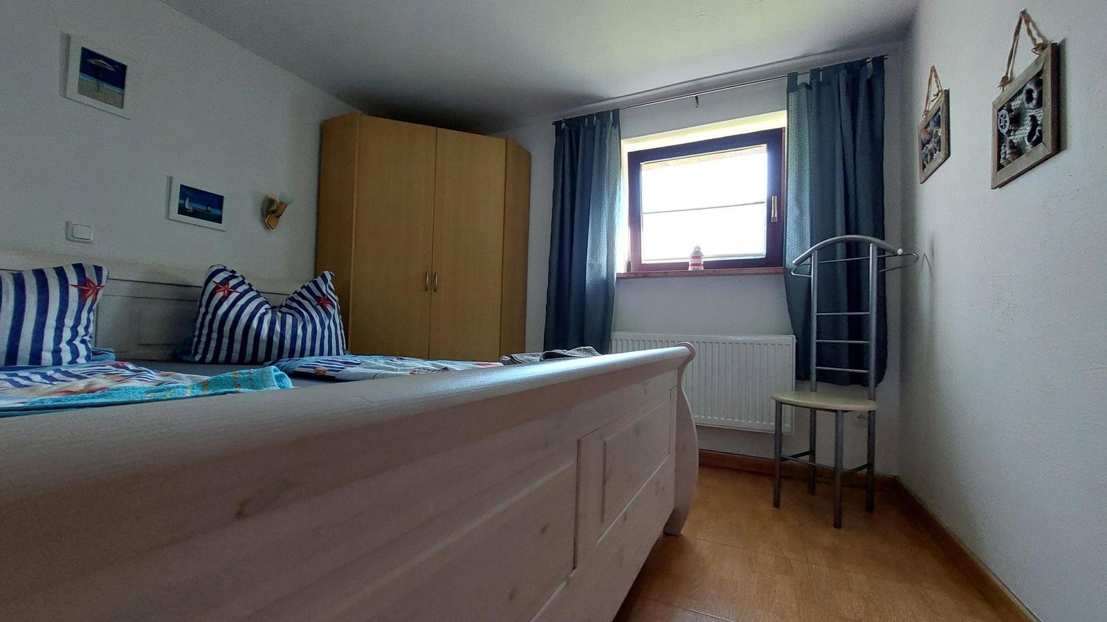 Schlafzimmer mit Bett, Kleiderschrank und Fenster mit Vorhängen.